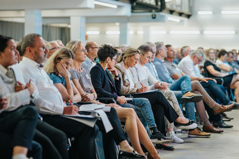 Eine große Gruppe von aufmerksamen Zuhörern sitzt in Reihen auf Stühlen und macht sich Notizen während einer Veranstaltung. Die Atmosphäre wirkt konzentriert und professionell. Eine große Gruppe von aufmerksamen Zuhörern sitzt in Reihen auf Stühlen und macht sich Notizen während einer Veranstaltung. Die Atmosphäre wirkt konzentriert und professionell.