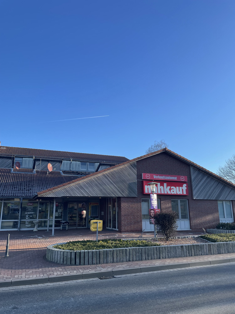 Ein "nahkauf"-Supermarkt mit roter Beschriftung befindet sich in einem flachen, braunen Backsteingebäude unter einem klaren, blauen Himmel. Vor dem Eingang erstreckt sich ein gepflasterter Bereich mit einer kleinen Grünfläche. Ein "nahkauf"-Supermarkt mit roter Beschriftung befindet sich in einem flachen, braunen Backsteingebäude unter einem klaren, blauen Himmel. Vor dem Eingang erstreckt sich ein gepflasterter Bereich mit einer kleinen Grünfläche.